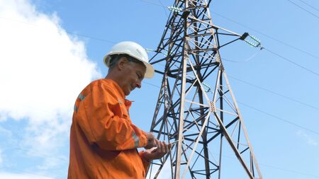 aged survey specialist types on smartphone under power linesの写真素材