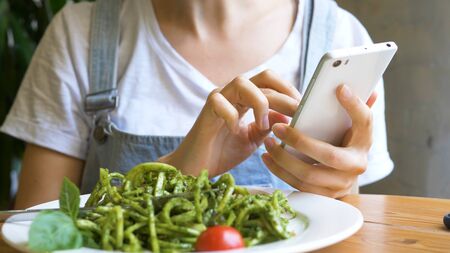 young woman in denim overalls types on modern smartphoneの写真素材