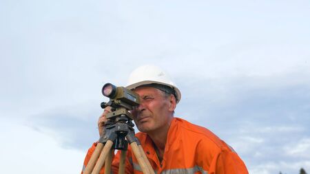 professional surveyor puts brown wooden tripod on groundの写真素材