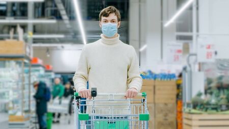A man in a medical mask stands in a supermarket with a food cart timelaps