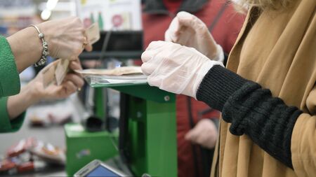 Woman at the supermarket checkout picks up change after shopping in rubber protective gloves. Safety measures against coronavirus infection.の写真素材