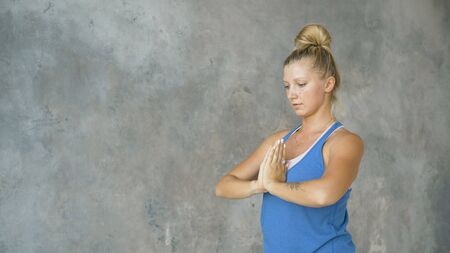 girl crouches in back folds arms in namaste, yoga workout in studioの写真素材