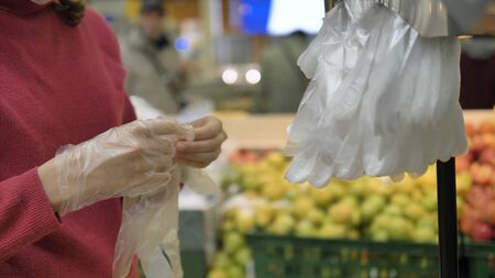 Coronavirus pandemic. A woman in a supermarket puts on disposable plastic gloves to protect against coronavirus, close-up. Precautions against the spread of the disease.の写真素材