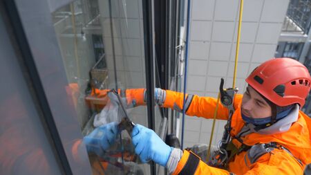 equipped window washer in a helmet and orange jumpsuit washes glass with a screed at high altitude...