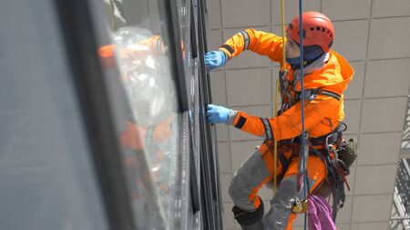 professional equipped climber in helmet and gloves washes windows with rubber screed high altitude,...