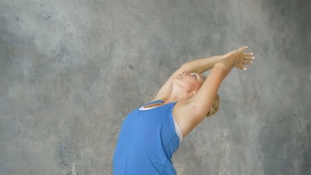 beautiful blonde girl demonstrates deflection in lower back folds hands in namaste, yoga training in light studioの写真素材