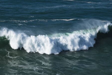 giant blue ocean wave breaks on the surface of the water with spray and foamの写真素材