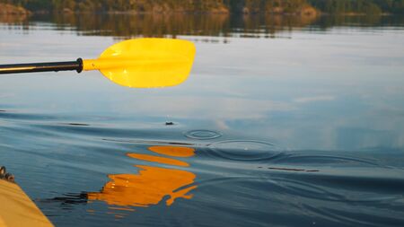 yellow paddle reflected in the lake on a kayak at sunset close-up, secluded vacationの写真素材
