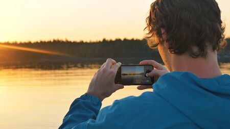 man photographs the sunset on a smartphone on the lake sitting in a kayak, outdoor activities aloneの写真素材