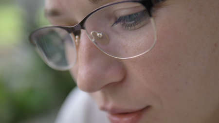 attractive young woman wearing stylish eyeglasses looks at something smiling on green blurred...