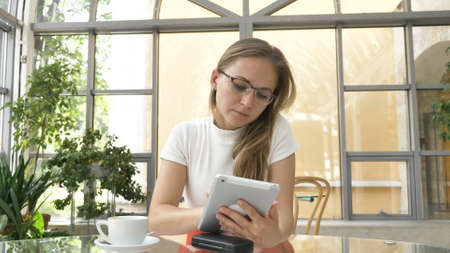 young blonde businesswoman takes off glasses from spectacles case to work on contemporary tablet at...