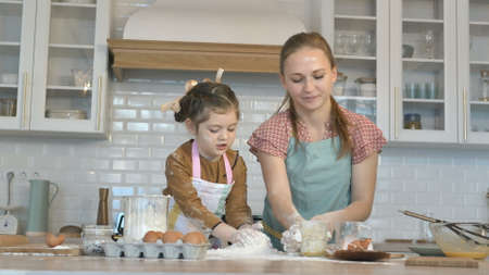 Cheerful little girl and young mommy throw flour making dough for tasty pie at large wooden table in contemporary kitchenの写真素材