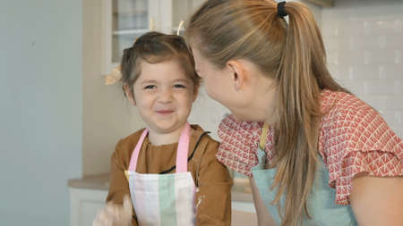 Cute little girl and cheerful mother in aprons play with white flour cooking cake together in contemporary kitchen closeupの写真素材