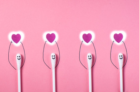 Cute cotton swabs with painted face and hands holding red hearts on pink background, valentines day concept.の写真素材