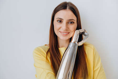 Attractive long haired lady with contemporary bionic prosthesis arm looks into camera standing on light grey background closeupの写真素材