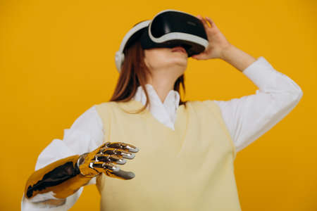 Concentrated blonde woman in vest with modern bionic arm and virtual reality headset plays game on...