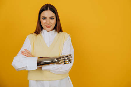 Woman with bionic prosthesis crosses arms by yellow wallの写真素材