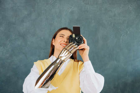 Young woman with metal bionic arm takes picture on grey