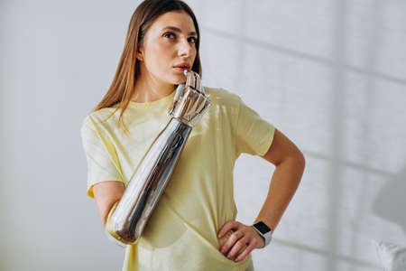 Thoughtful woman with metal bionic prosthesis arm in roomの写真素材