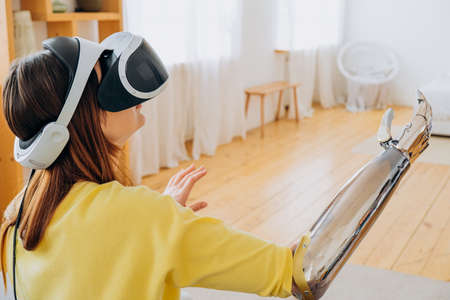 Woman with bionic arm and VR headset plays game in roomの写真素材