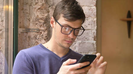 Young man in glasses holds smartphone and reads informationの写真素材
