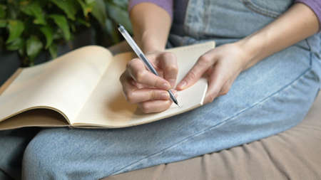 Young student holds copybook on knees and writes notesの写真素材
