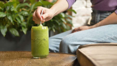Woman hand takes metal straw and stirs vegetable cocktailの写真素材