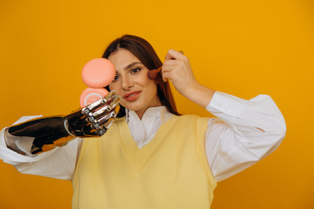 Attractive woman with bionic arm applies makeup on yellowの写真素材