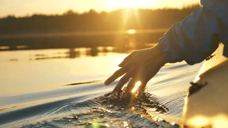 man puts fingers down lake kayaking against backdrop of golden sunset, unity harmony natureの写真素材