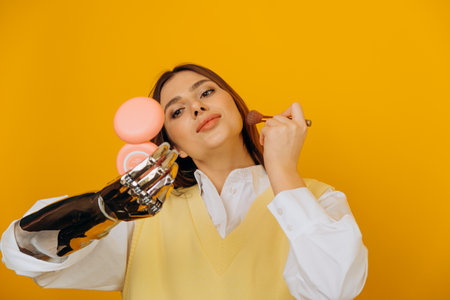 Attractive woman with bionic arm applies makeup on yellowの写真素材