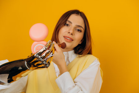 Attractive woman with bionic arm applies makeup on yellowの写真素材