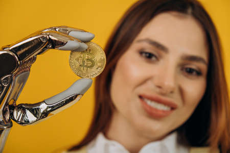 Lady with shiny bionic arm holds golden bitcoin on yellowの写真素材