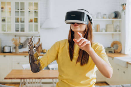 Woman with bionic arm and VR headset dances in kitchenの写真素材
