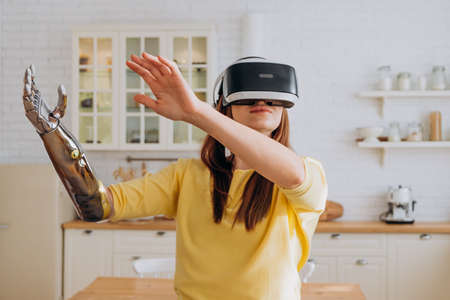 Woman with bionic arm and VR headset dances in kitchenの写真素材