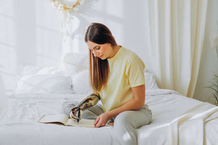Woman writes in notebook with bionic arm sitting on bedの写真素材