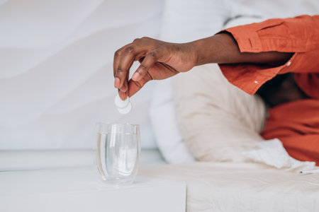 Sick African man throws two fever pills into a glass tumbler close-upの写真素材