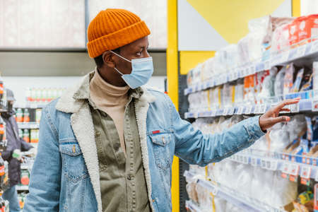 African-American man in a medical mask in a supermarket chooses productsの写真素材