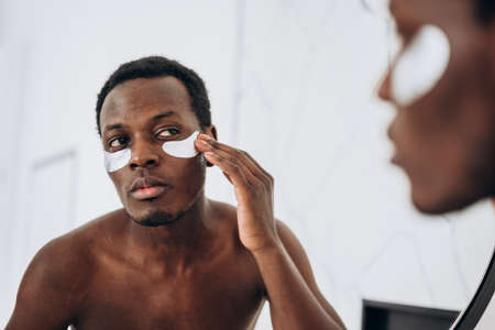 Handsome African-American guy uses eye patches in bathroomの写真素材