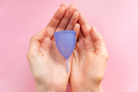Young woman holds menstrual cup on pink backgroundの写真素材