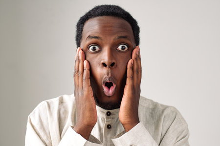 Shocked African-American man holds cheek on light greyの写真素材
