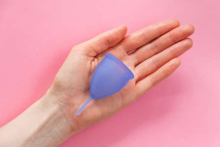 Woman palm holds purple menstrual cup on pink backgroundの写真素材