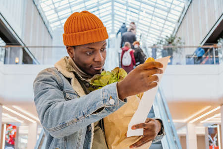 Surprised black man looks at receipt total with food in mallの写真素材