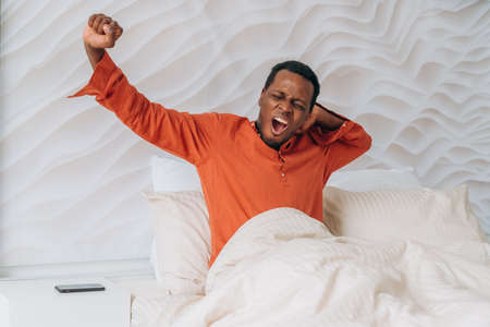 African-American guy awakes stretching in comfortable bedの写真素材
