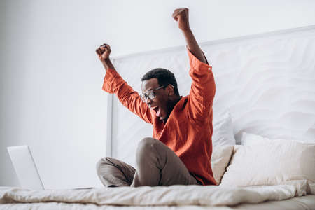 African-American guy puts hands up sitting near laptopの写真素材