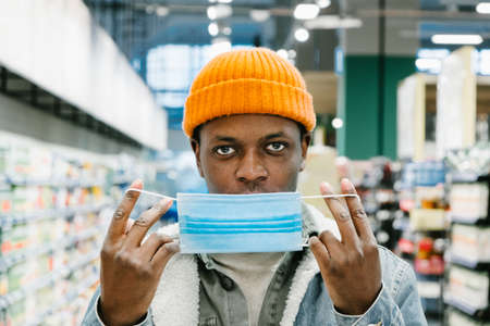 African-American man puts on blue disposable mask in storeの写真素材