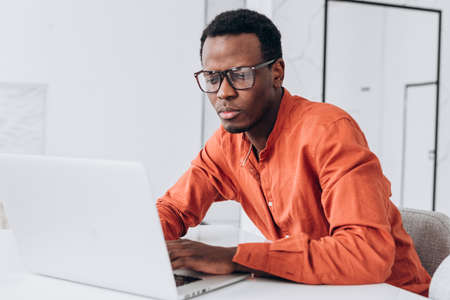 Young African-American guy works on modern laptop at tableの写真素材