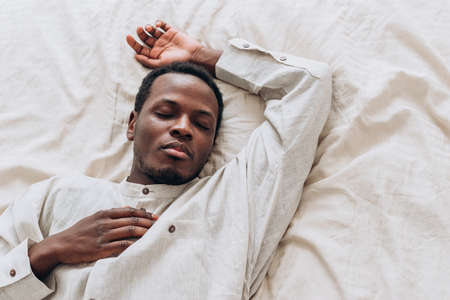 Calm African-American man in shirt sleeps on comfortable bedの写真素材