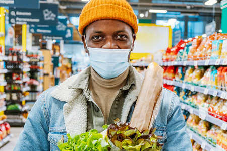 Happy African-American man in mask holds salads in storeの写真素材