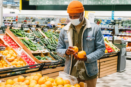 Young African-American customer takes orange fruits in storeの写真素材