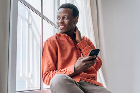 Black guy looks out of window holding phone in roomの写真素材